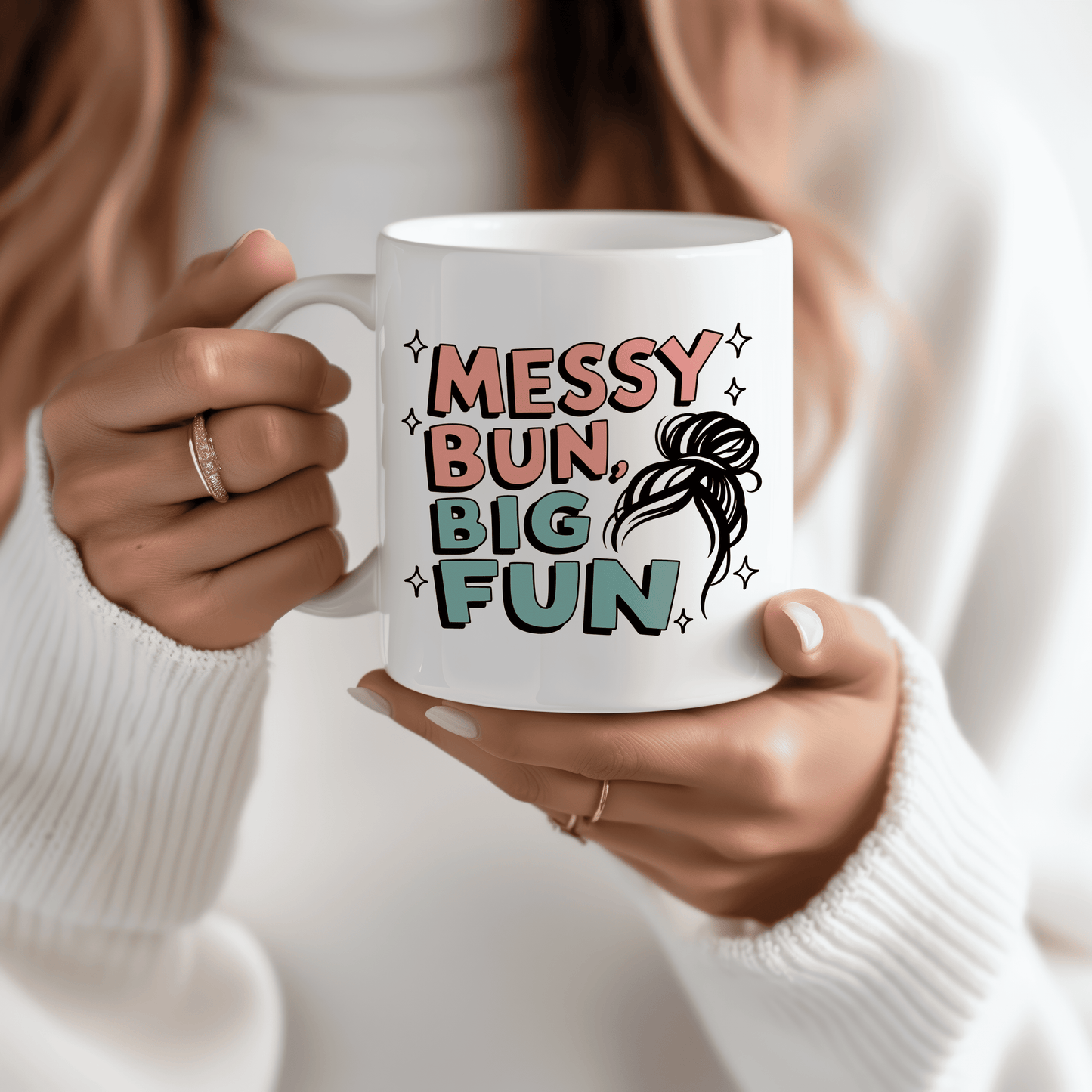 Woman holding white ceramic mug with pastel lettering that says “Messy Bun, Big Fun” and a fun sketch of a messy hairstyle