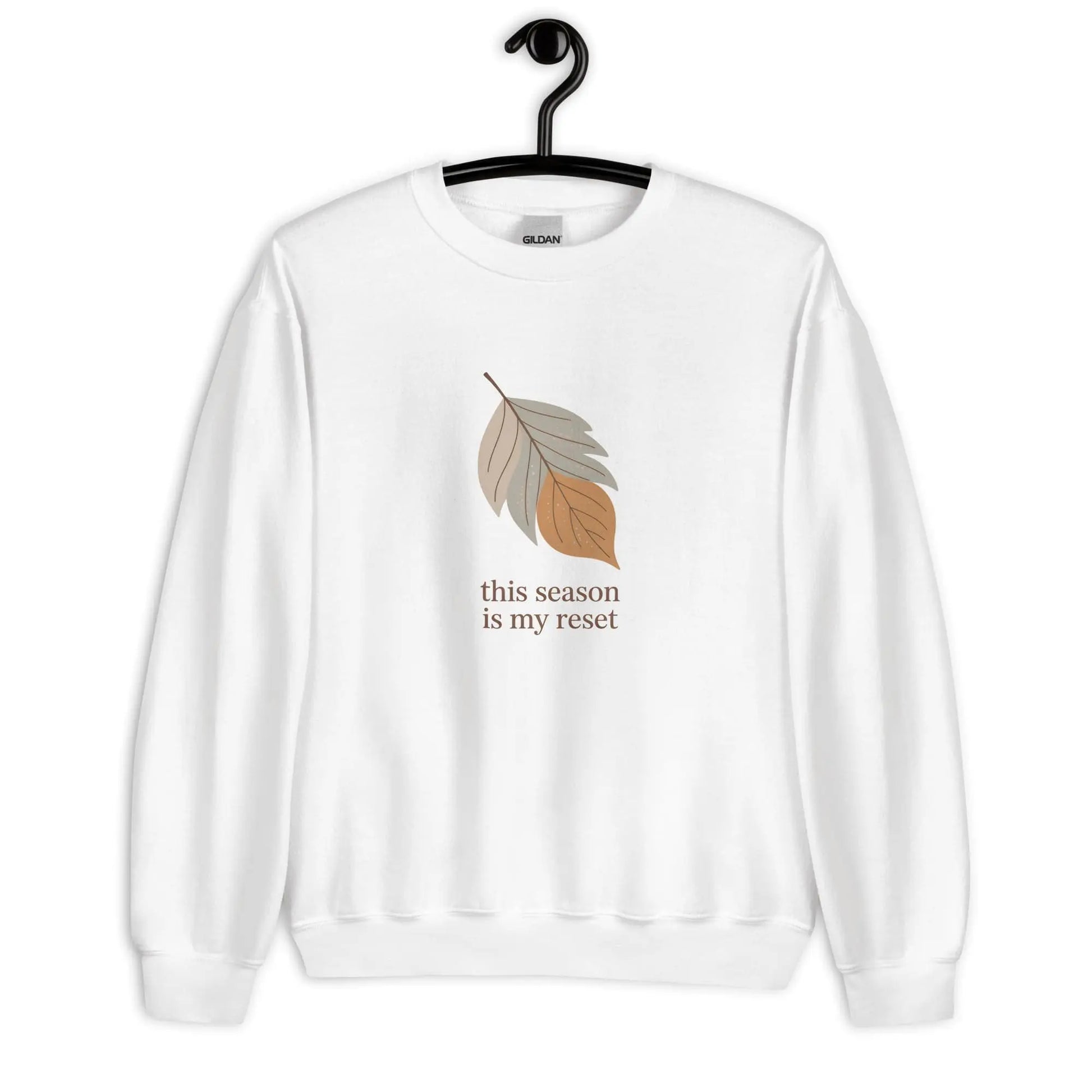 White sweatshirt with leaf graphic and text 'this season is my reset' on a hanger against a white background