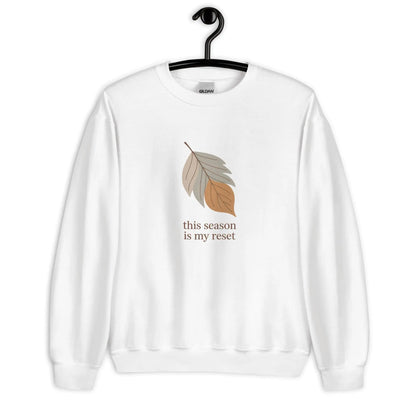 White sweatshirt with leaf graphic and text 'this season is my reset' on a hanger against a white background