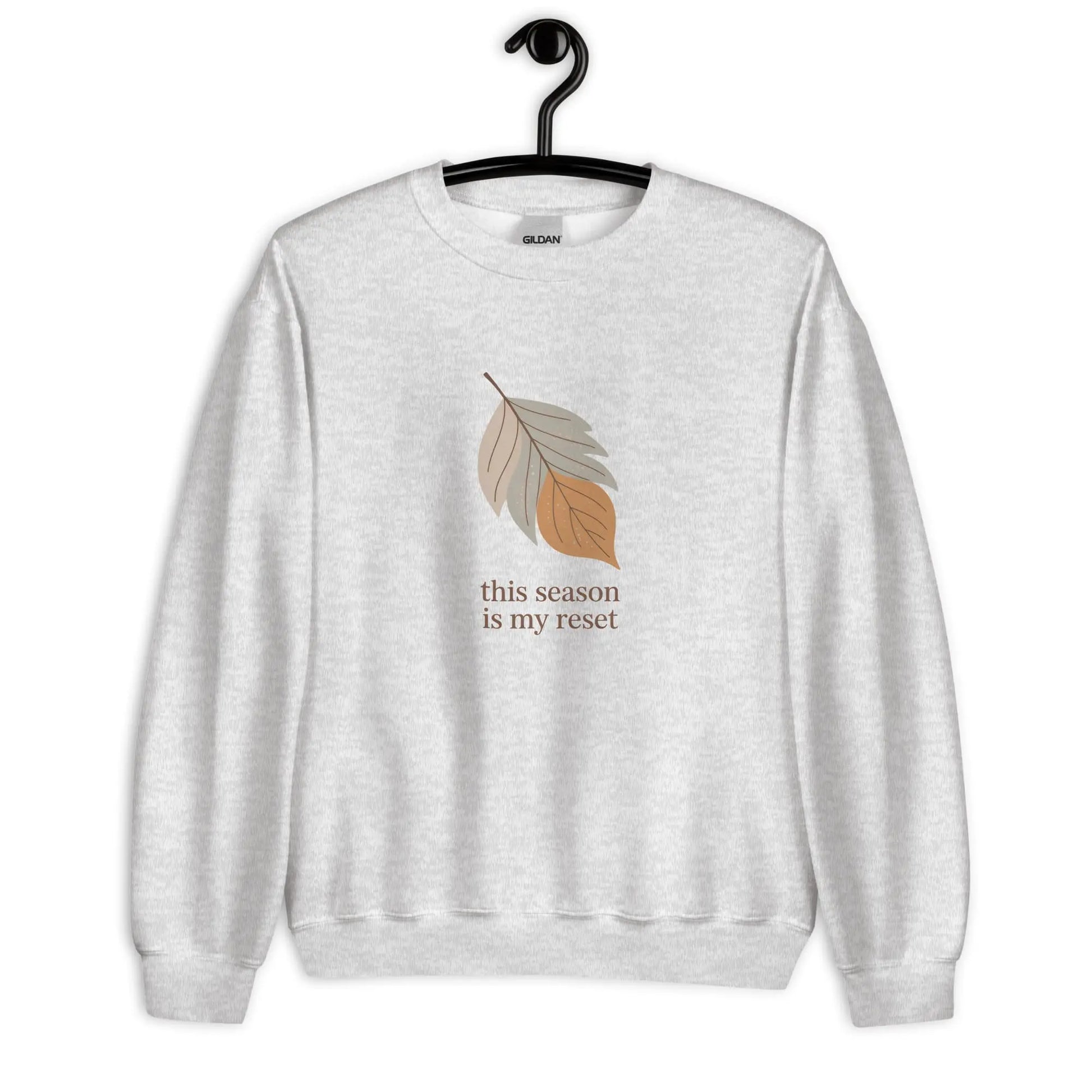 Gray sweatshirt with leaf graphic and text 'this season is my reset' on a hanger against a white background