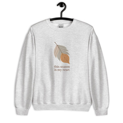 Gray sweatshirt with leaf graphic and text 'this season is my reset' on a hanger against a white background