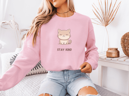 Woman wearing a pastel pink sweatshirt with a cute smiling cat and “Stay Kind” quote
