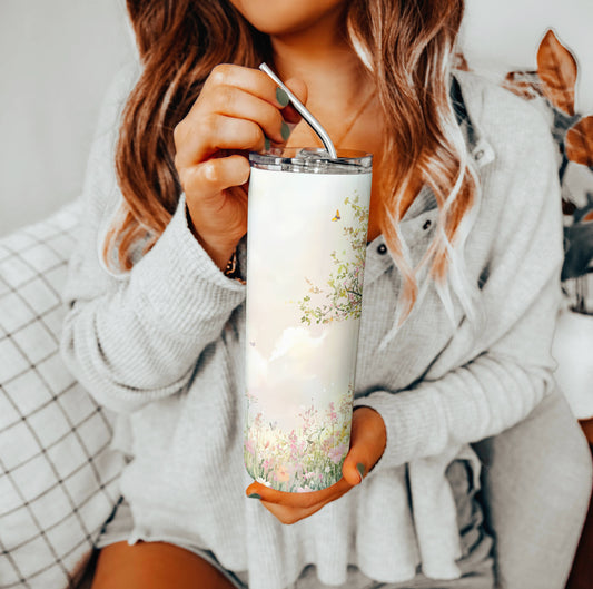 Woman sitting on a couch, holding a tall pastel floral tumbler with a metal straw; cozy indoor setting with soft tones and relaxed vibes.