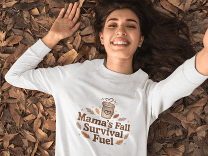 Woman wearing a white sweatshirt with 'Mama's Fall Survival Fuel' text, lying on fall leaves.