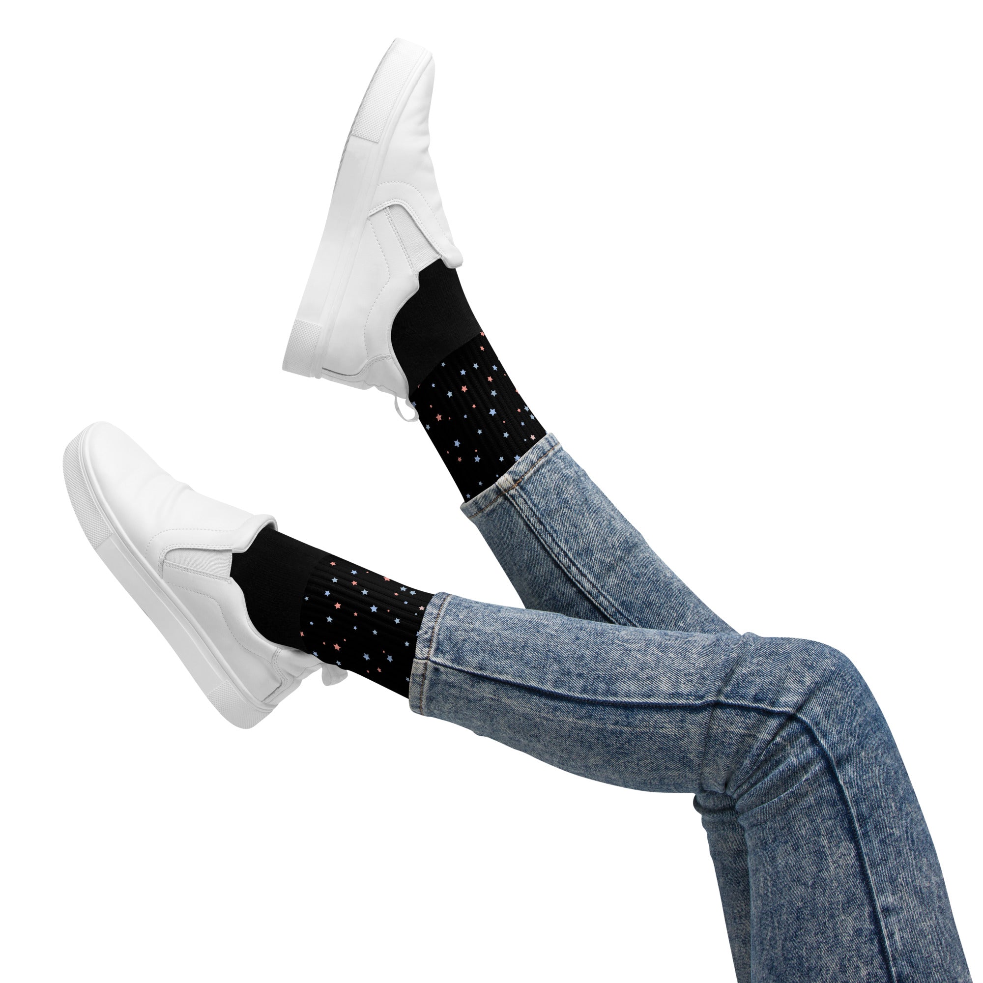 Person wearing black socks with a red and blue little stars, paired with white sneakers and jeans, playfully lifting legs in the air against a white background — cozy and energetic vibe.