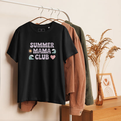 Black t-shirt with pastel "Summer Mama Club" design hanging on a white rack with cozy boho decor in the background.