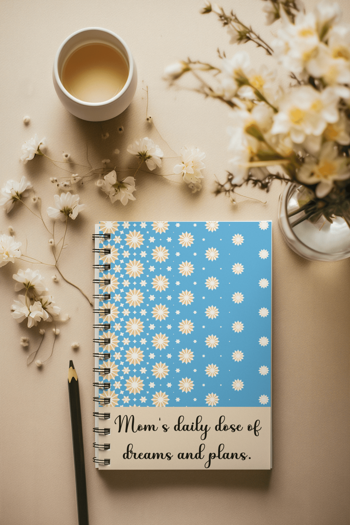 Blue notebook with yellow and white stars design and “Mom’s daily dose of dreams and plans” quote – cozy flatlay with tea and flowers, perfect gift for moms