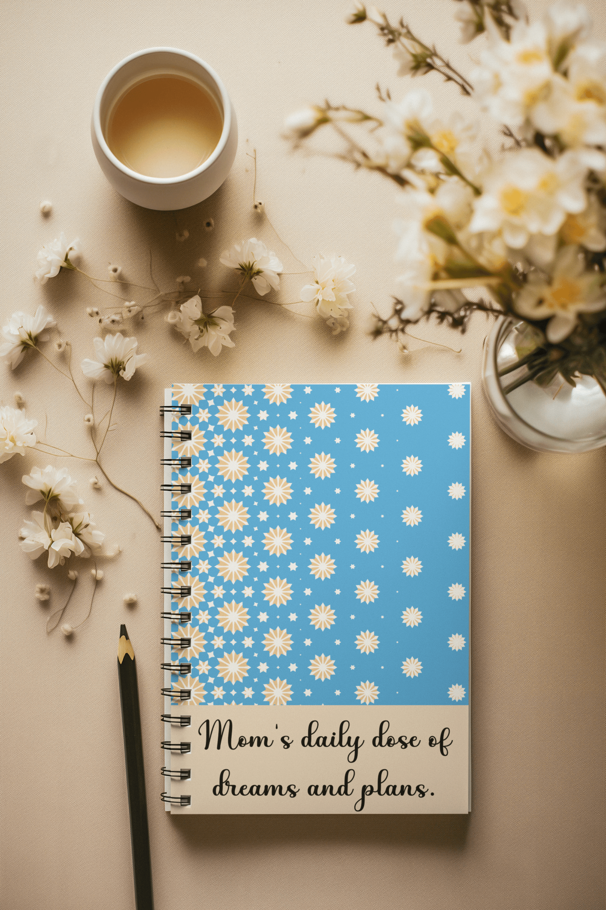 Blue notebook with yellow and white stars design and “Mom’s daily dose of dreams and plans” quote – cozy flatlay with tea and flowers, perfect gift for moms