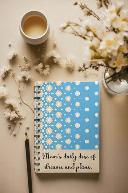 Blue notebook with yellow and white stars design and “Mom’s daily dose of dreams and plans” quote – cozy flatlay with tea and flowers, perfect gift for moms