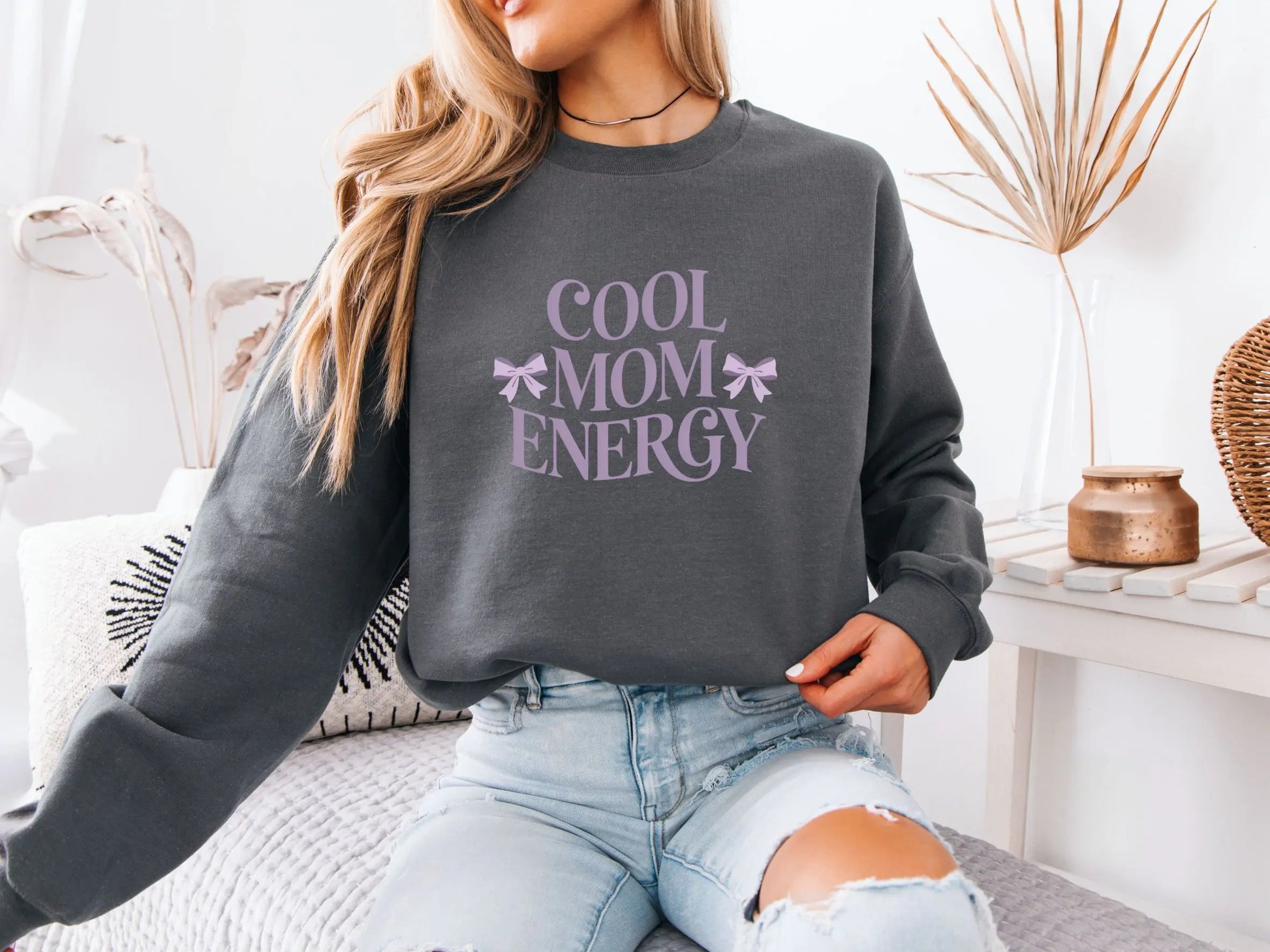 Woman wearing a grey “Cool Mom Energy” sweatshirt in a cozy home setting