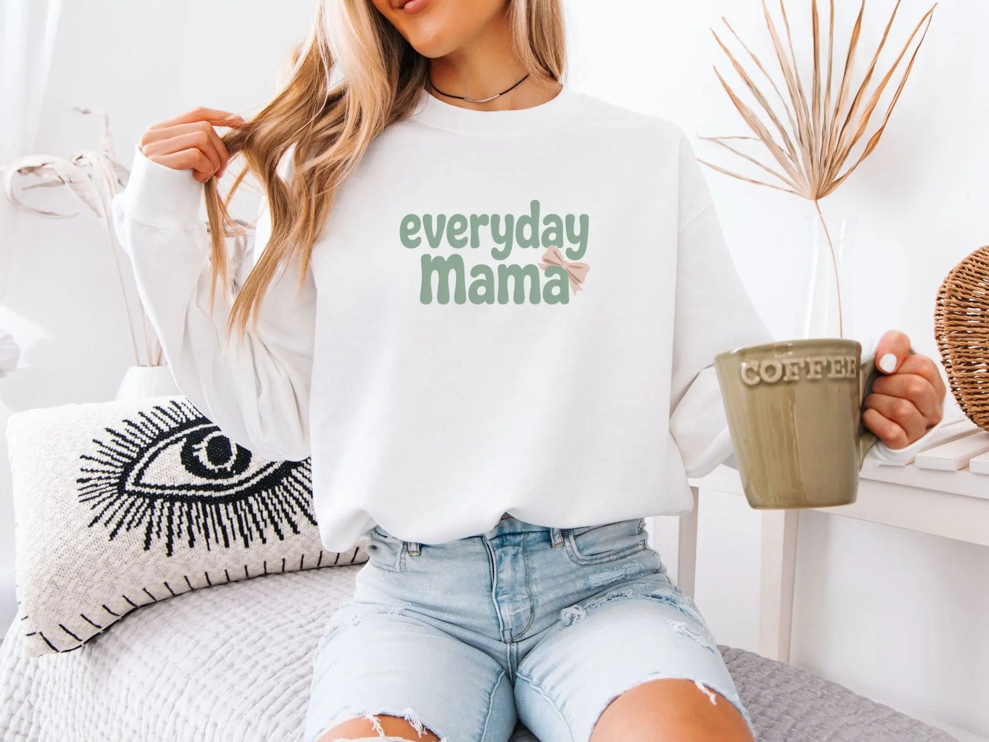 Model wearing white Everyday Mama sweatshirt with green lettering and a blush pink bow, minimalist mom look.