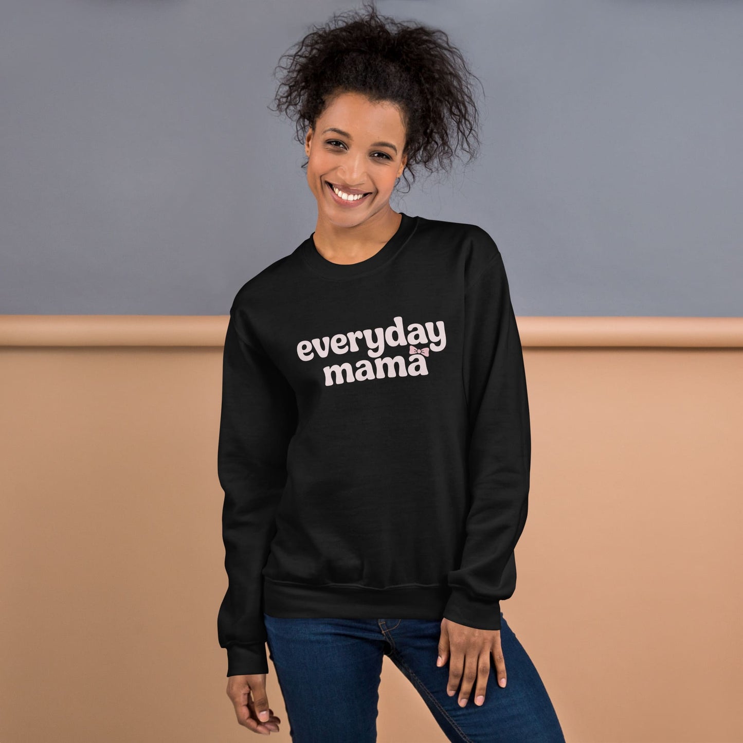 Woman wearing a black sweatshirt with 'everyday mama' text against a neutral background