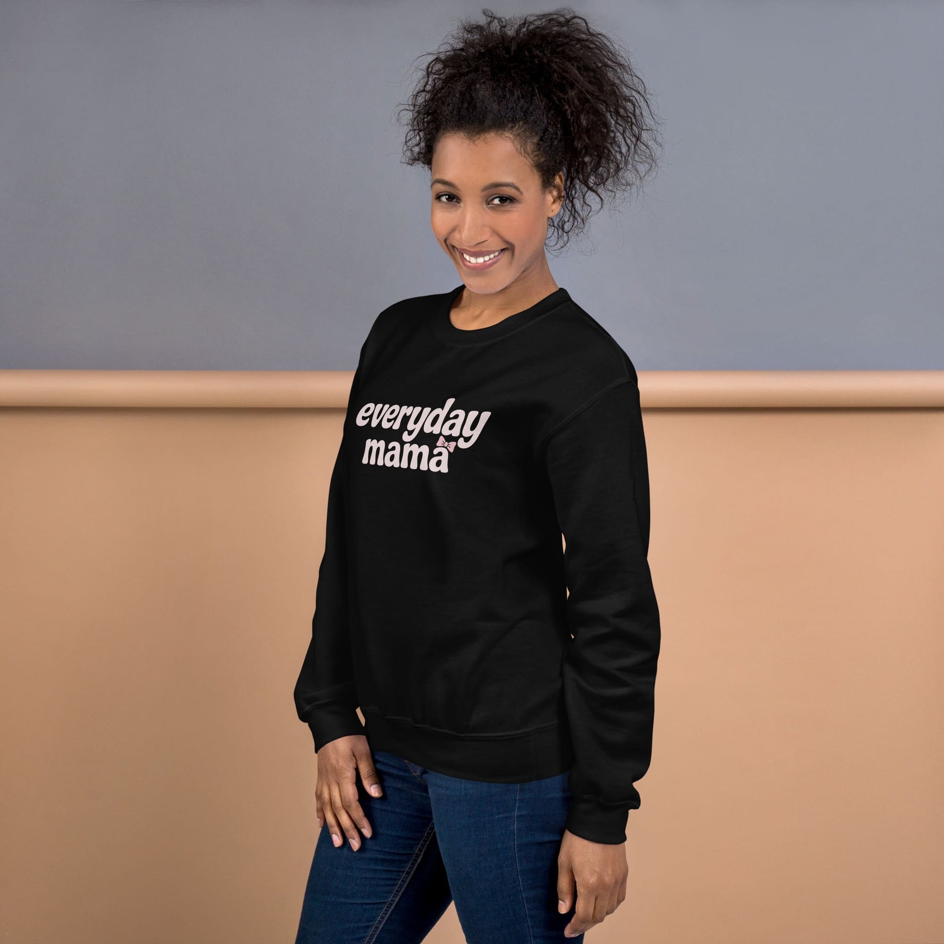 Woman wearing a black sweatshirt with 'everyday mama' text against a neutral background