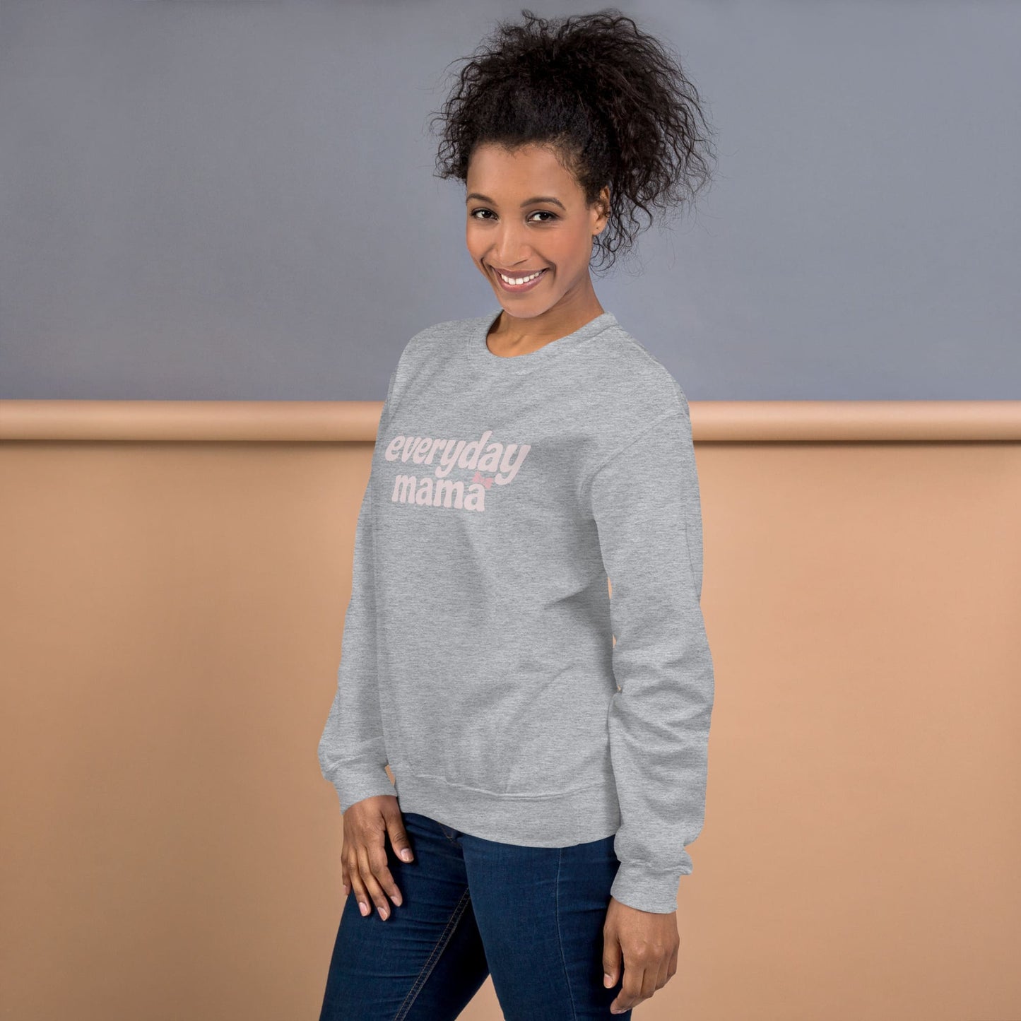 Woman wearing a gray sweatshirt with 'everyday mama' text against a plain background