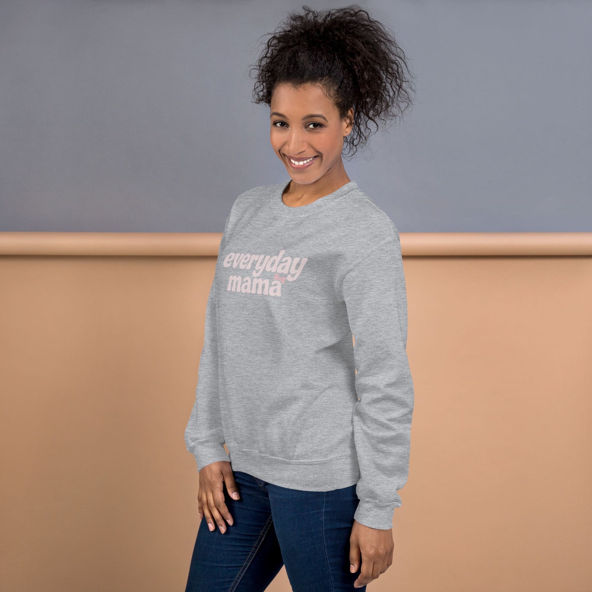 Woman wearing a gray sweatshirt with 'everyday mama' text against a plain background