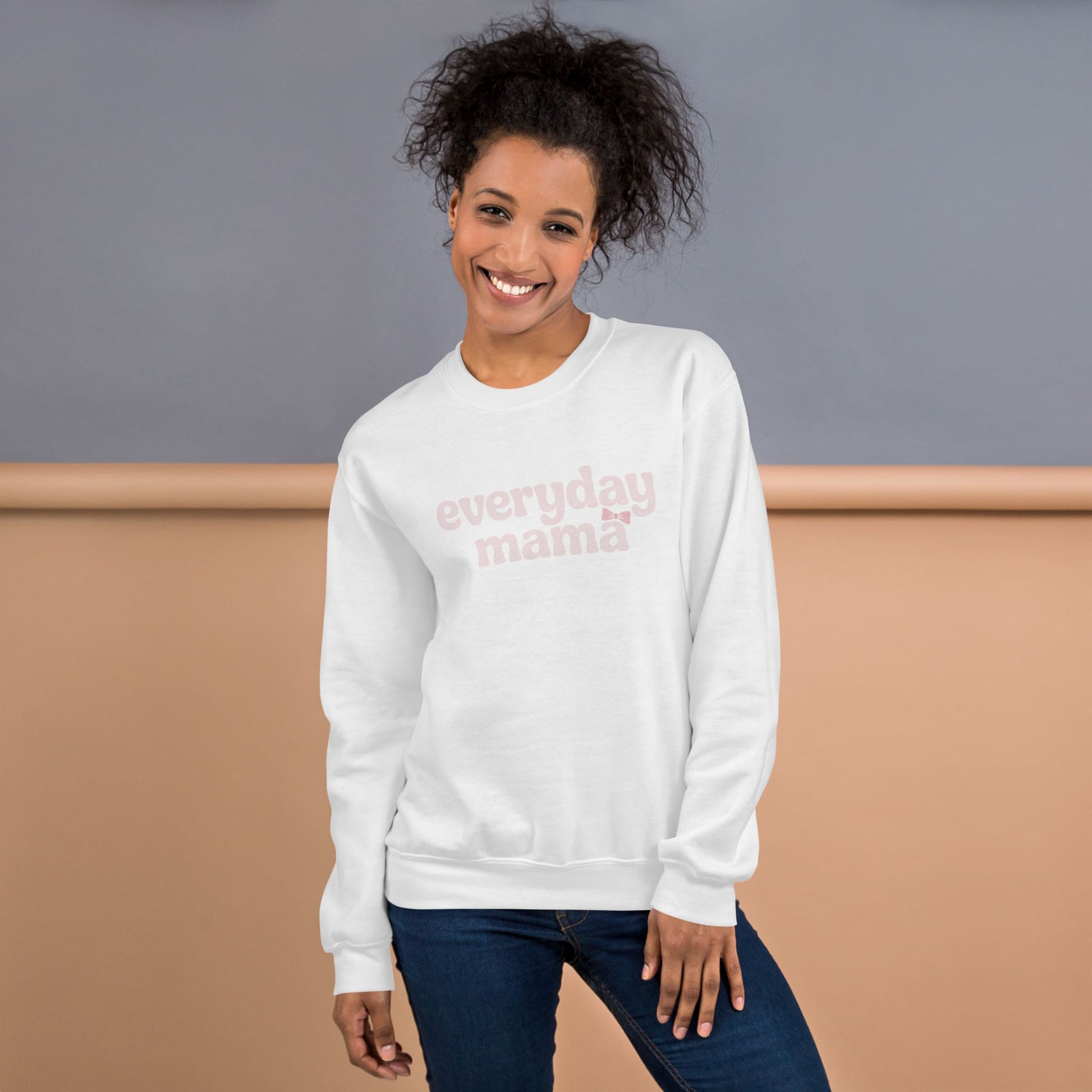 Woman wearing a white sweatshirt with 'everyday mama' text against a gray and beige background