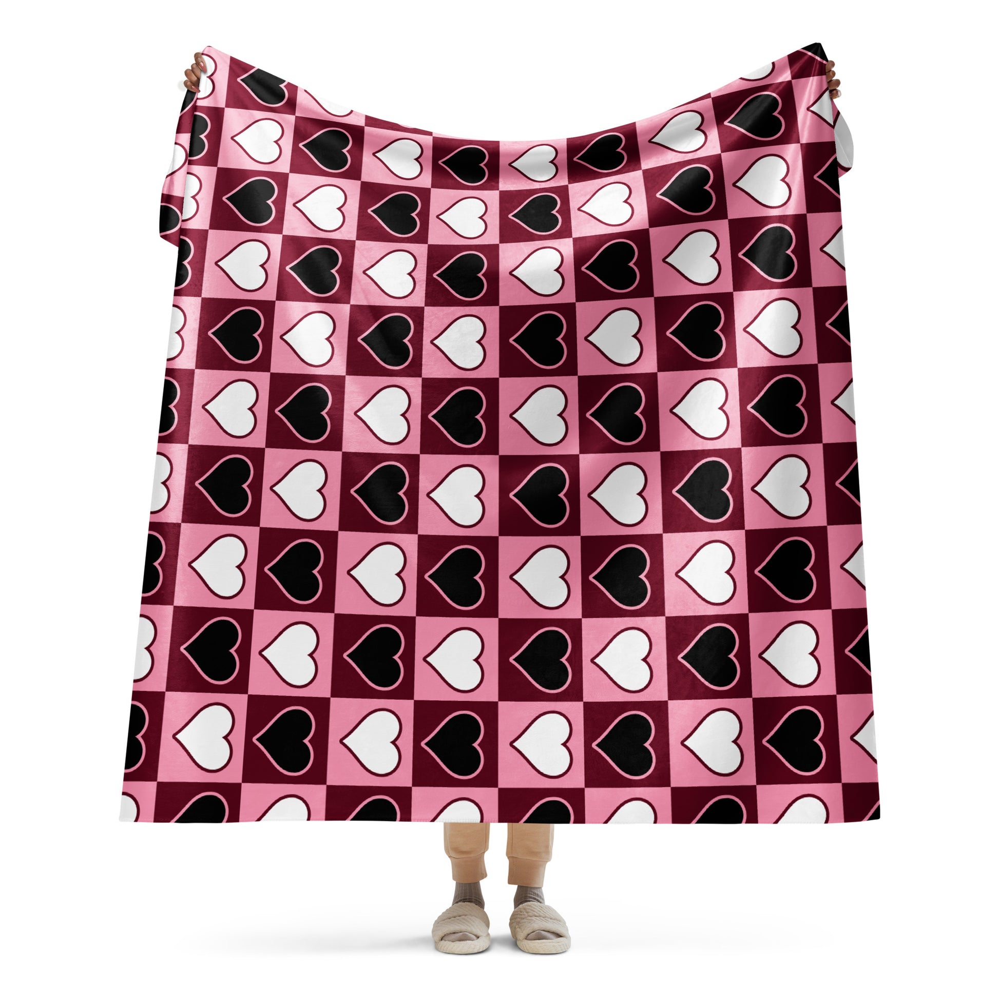 Full view of large heart pattern sherpa blanket held up by a person, showing the full design in pink, white, and black