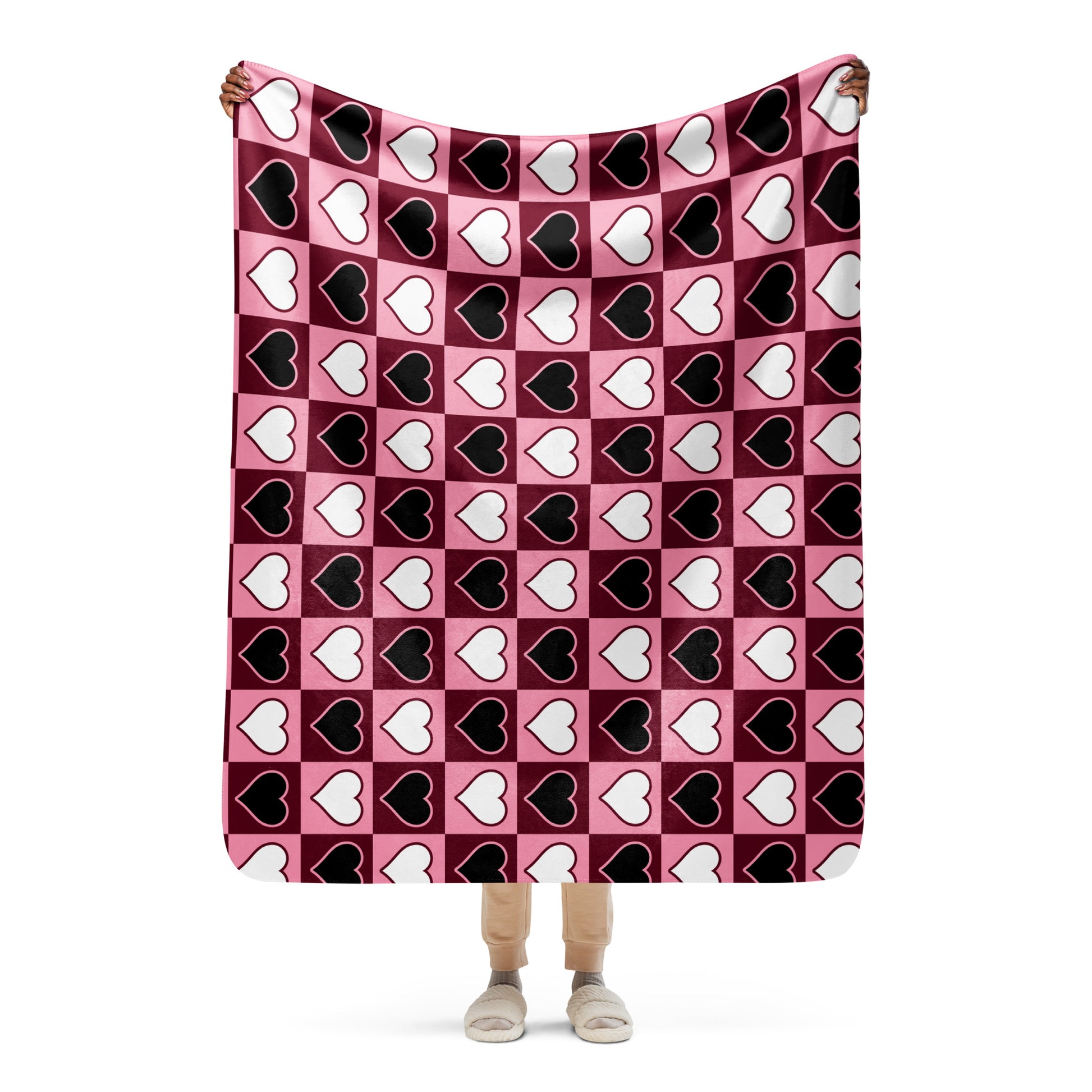 Full view of medium heart pattern sherpa blanket held up by a person, showing the full design in pink, white, and black