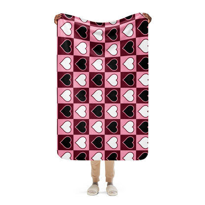 Full view of small heart pattern sherpa blanket held up by a person, showing the full design in pink, white, and black
