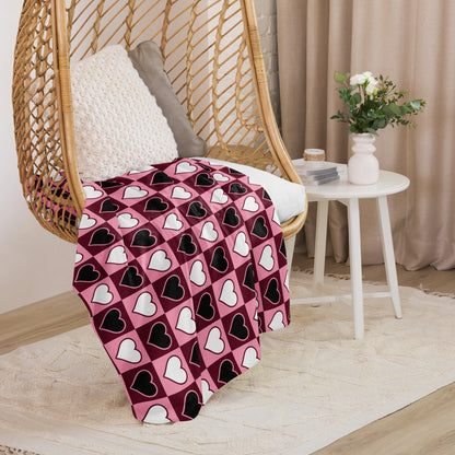 Small size heart pattern throw blanket in pink, black, and white, folded over a cozy rattan hanging chair 