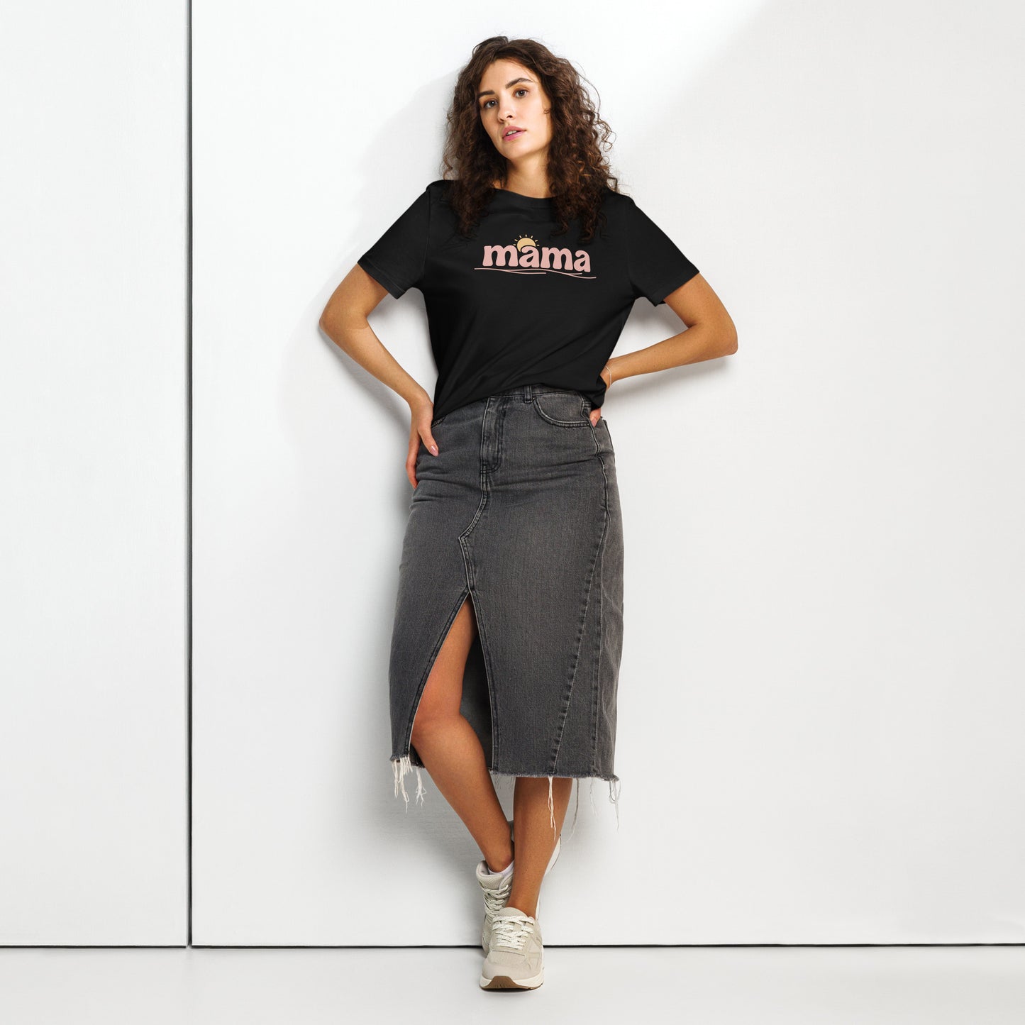 Woman wearing black ‘mama’ t-shirt with pastel sun design, styled with denim skirt, standing against white wall