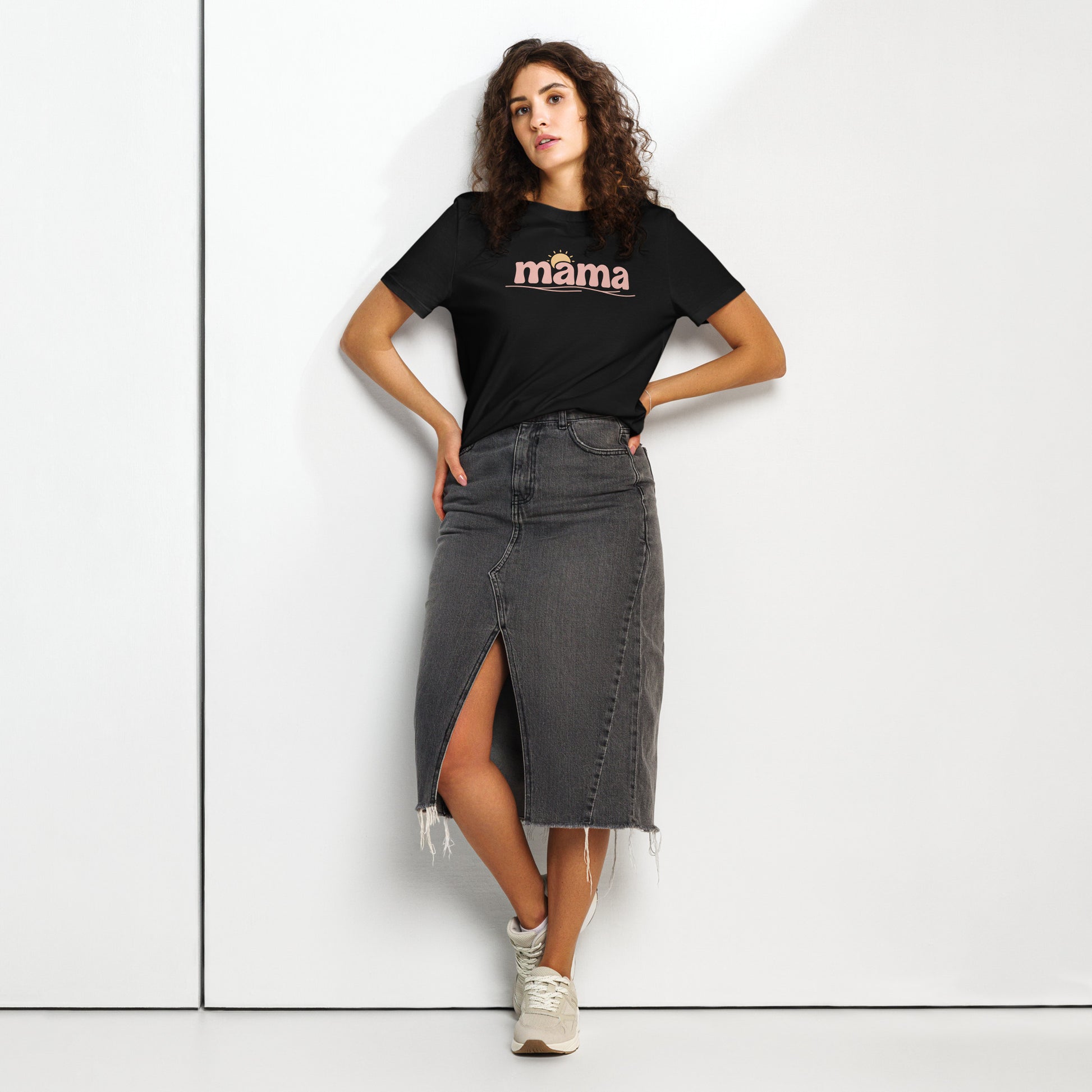 Woman wearing black ‘mama’ t-shirt with pastel sun design, styled with denim skirt, standing against white wall