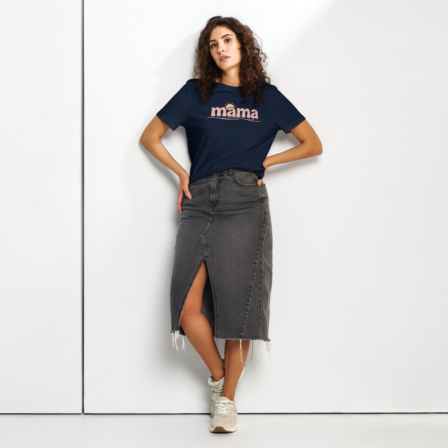 Woman wearing navy blue ‘mama’ t-shirt with pastel sun design, styled with denim skirt, standing against white wall