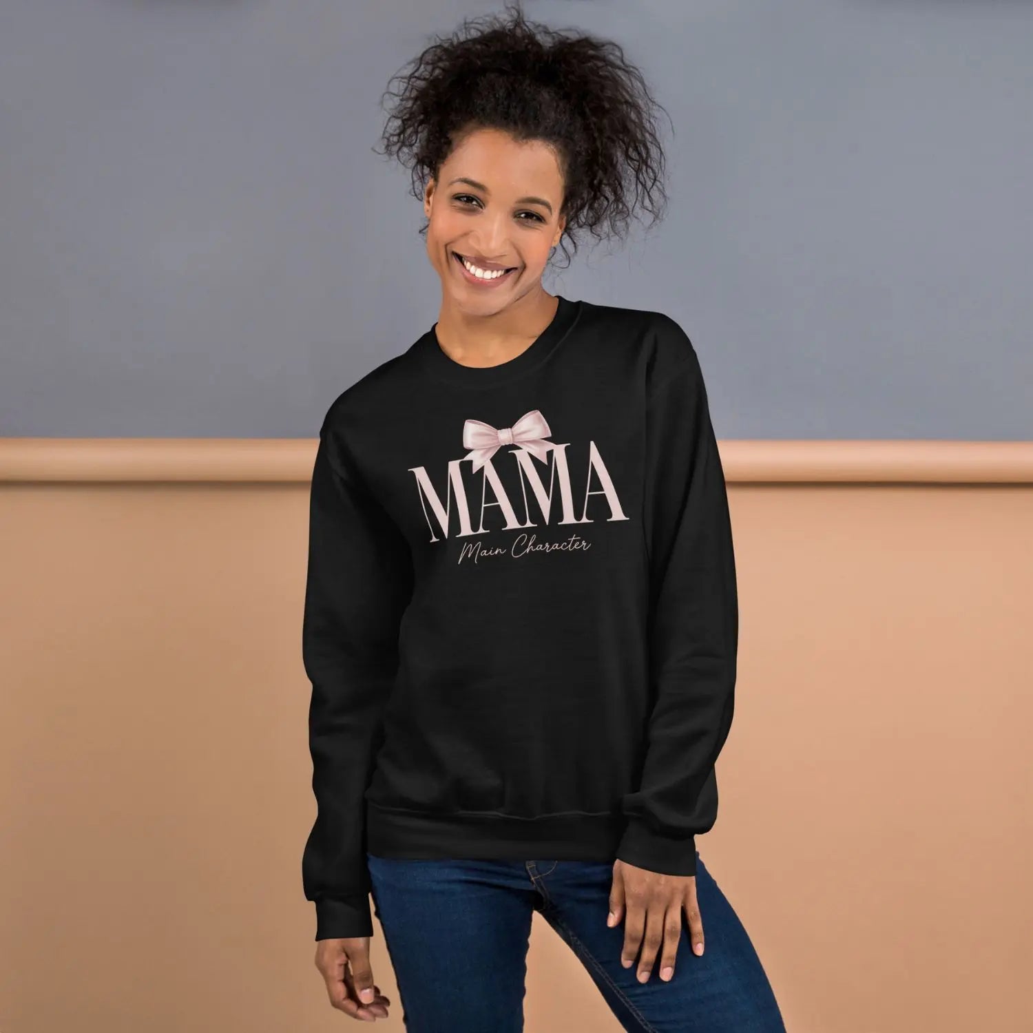 Woman wearing a black sweatshirt with 'MAMA Main Character' text and a bow graphic.