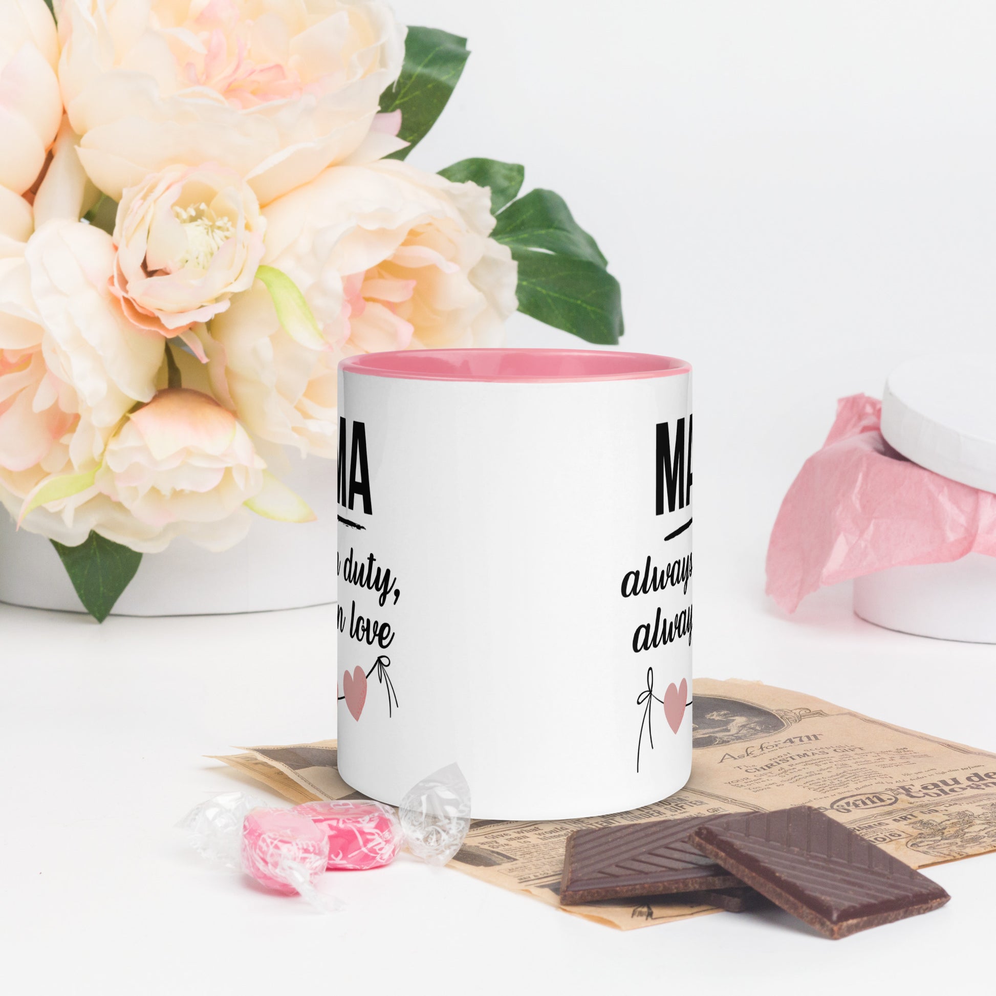 White ceramic mug with pink handle and inner color – “MAMA always on duty, always in love” quote with heart design, styled with chocolate and flowers - back view