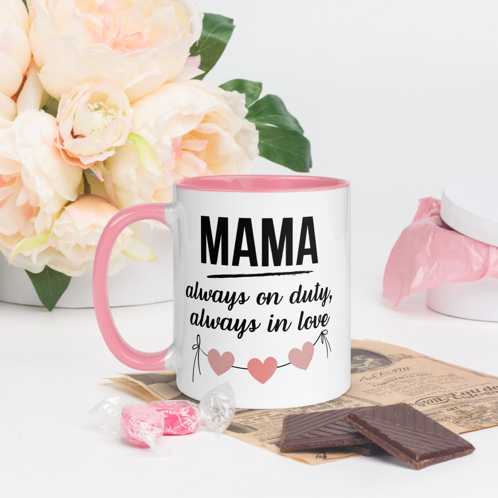White ceramic mug with pink handle and inner color – “MAMA always on duty, always in love” quote with heart design, styled with chocolate and flowers - left side

