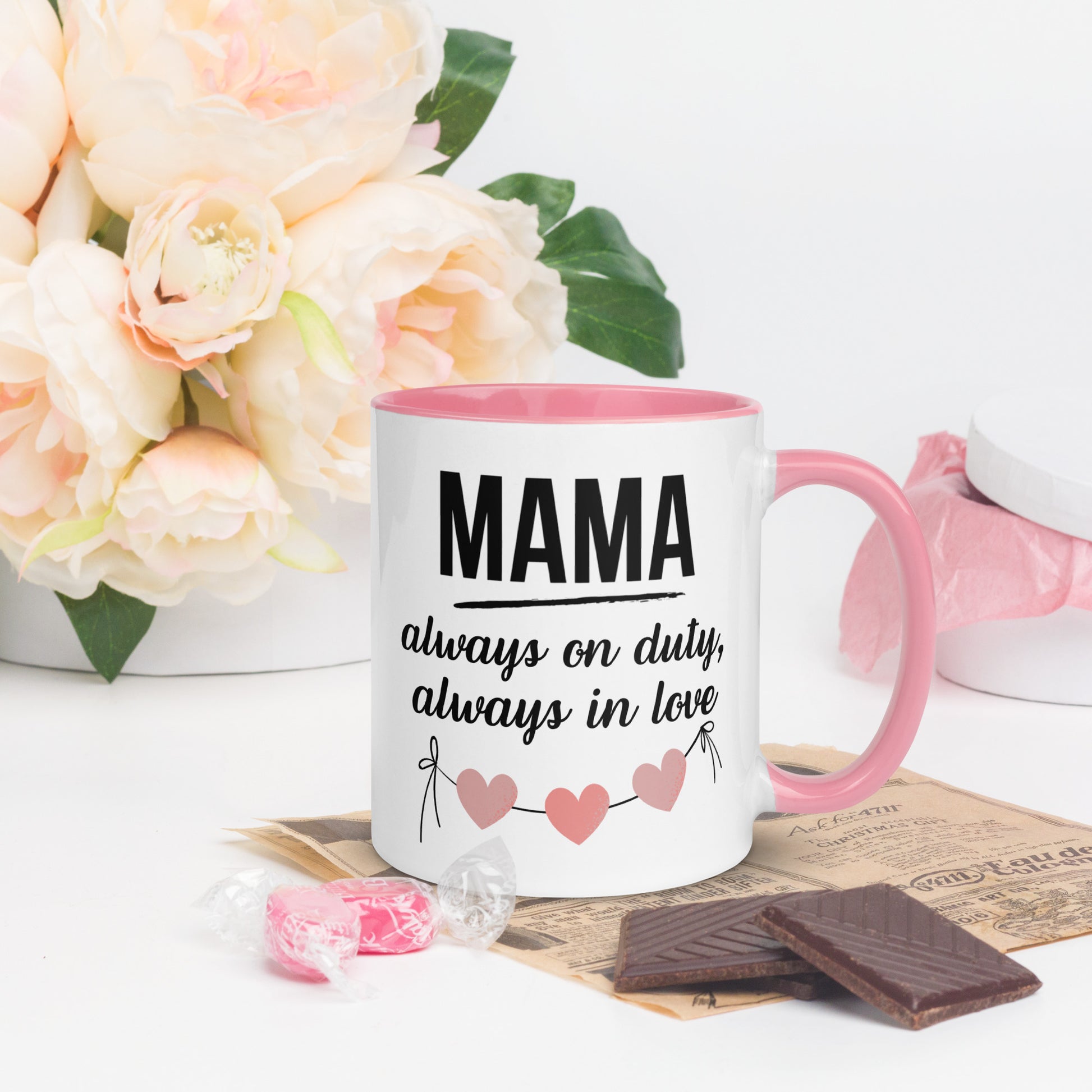 White ceramic mug with pink handle and inner color – “MAMA always on duty, always in love” quote with heart design, styled with chocolate and flowers - right side
