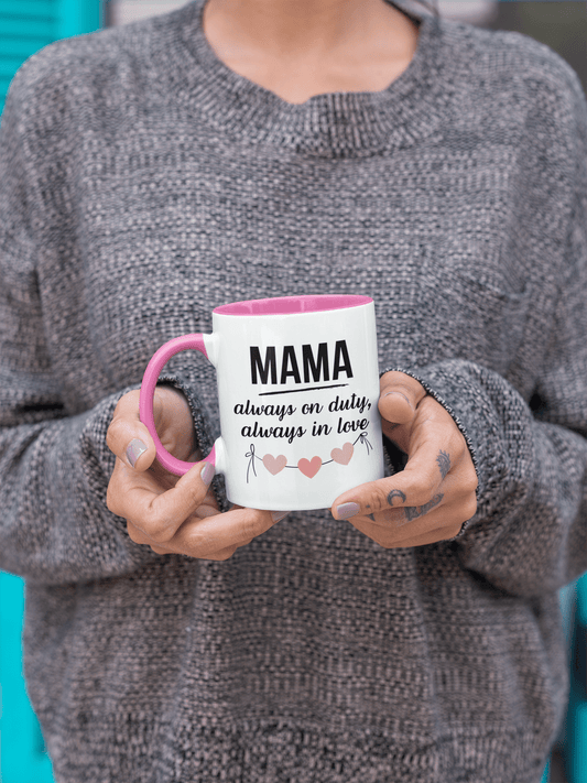A woman holding white ceramic mug with pink handle and inner color – “MAMA always on duty, always in love” quote with heart design