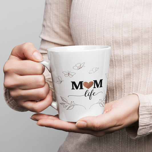 Woman holding white 12 oz latte mug with 'Mom Life' design and butterfly accents.