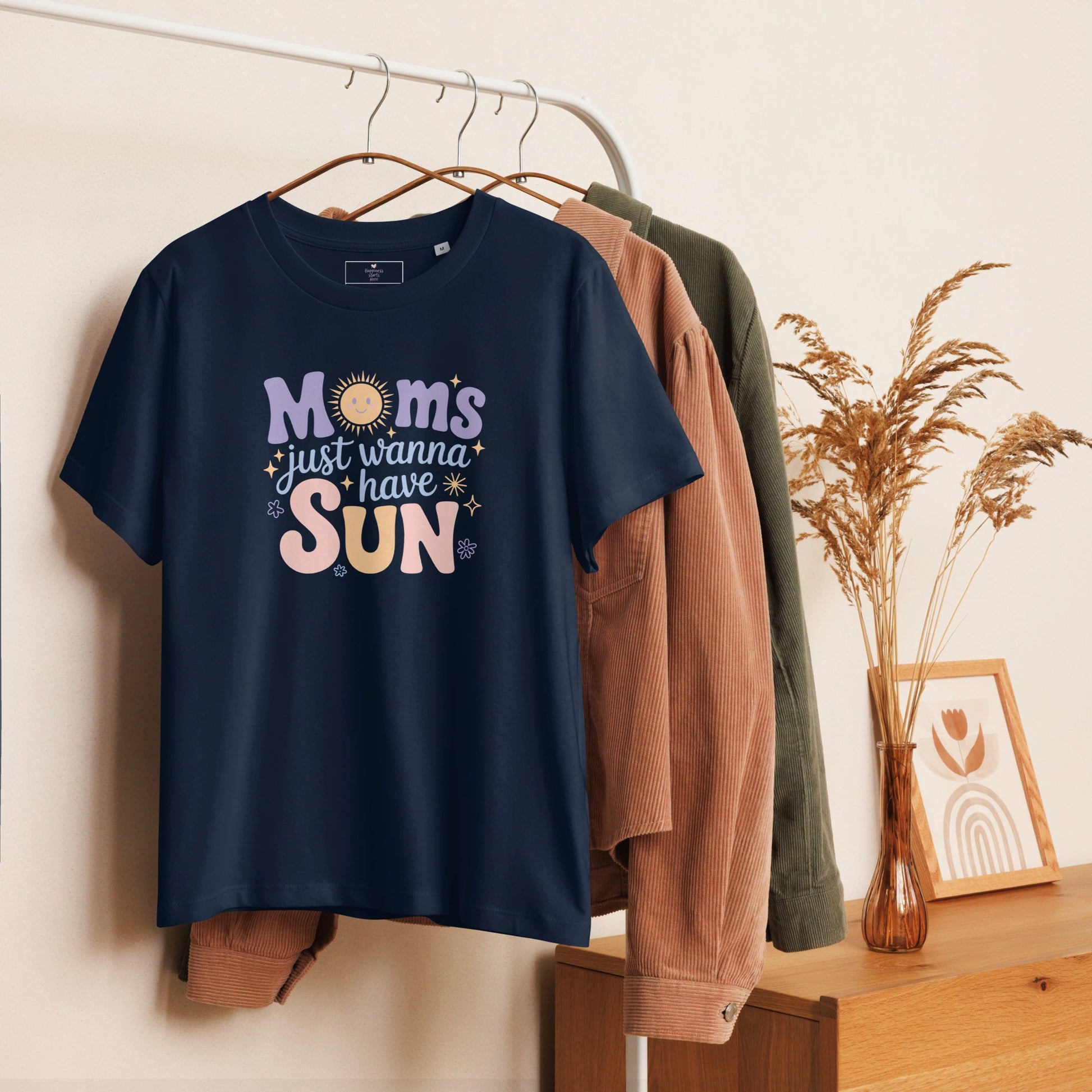 Navy blue t-shirt with “Moms Just Wanna Have Sun” pastel design hanging on clothing rack – cozy styled product photo for summer t-shirt for moms