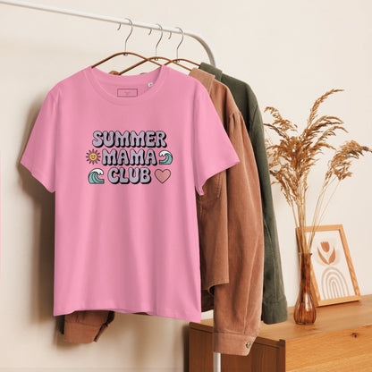 Pink t-shirt with pastel "Summer Mama Club" design hanging on a white rack with cozy boho decor in the background.