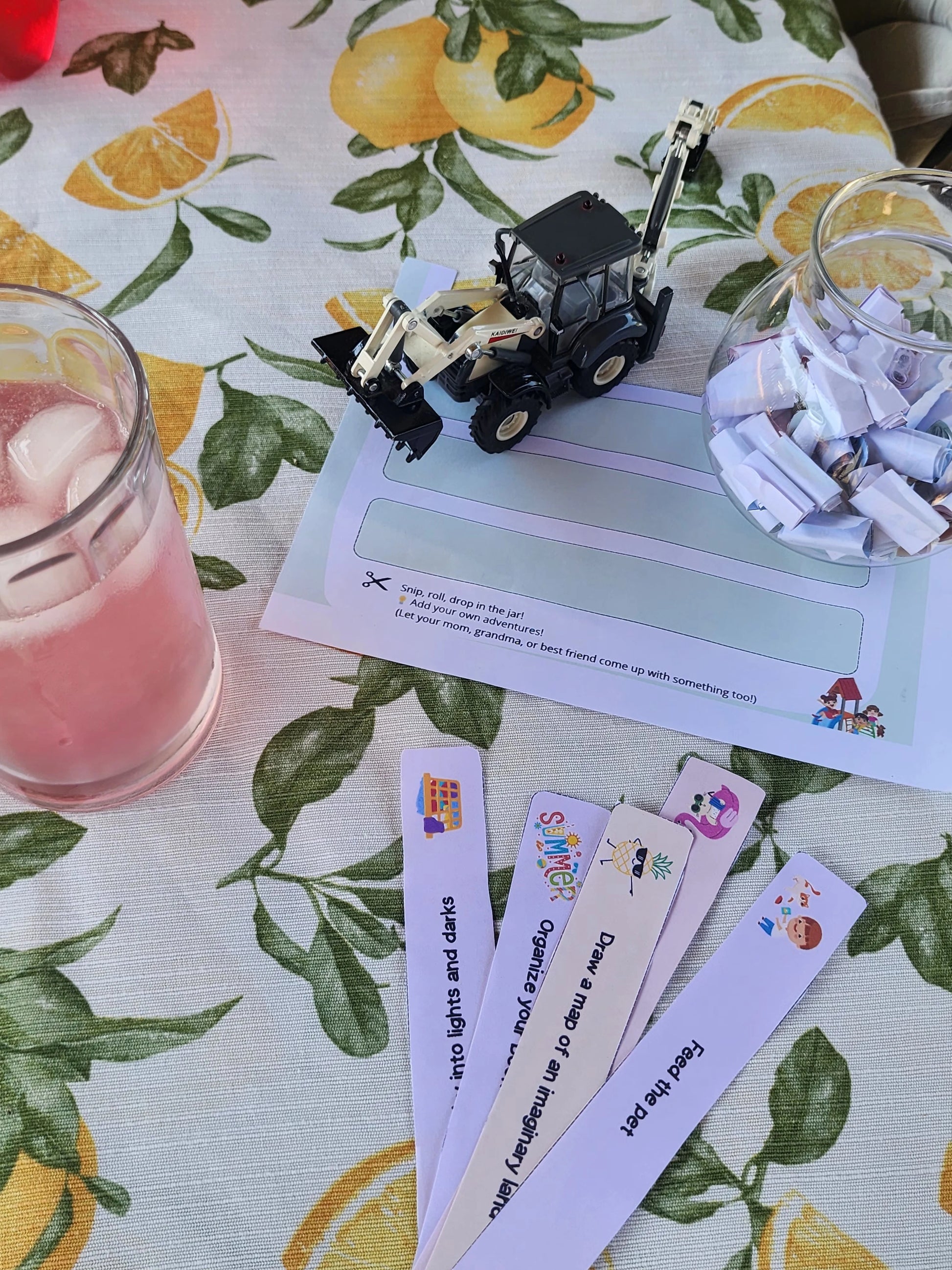 Printable activity strips and a filled glass jar on a table with a toy tractor and pink drink