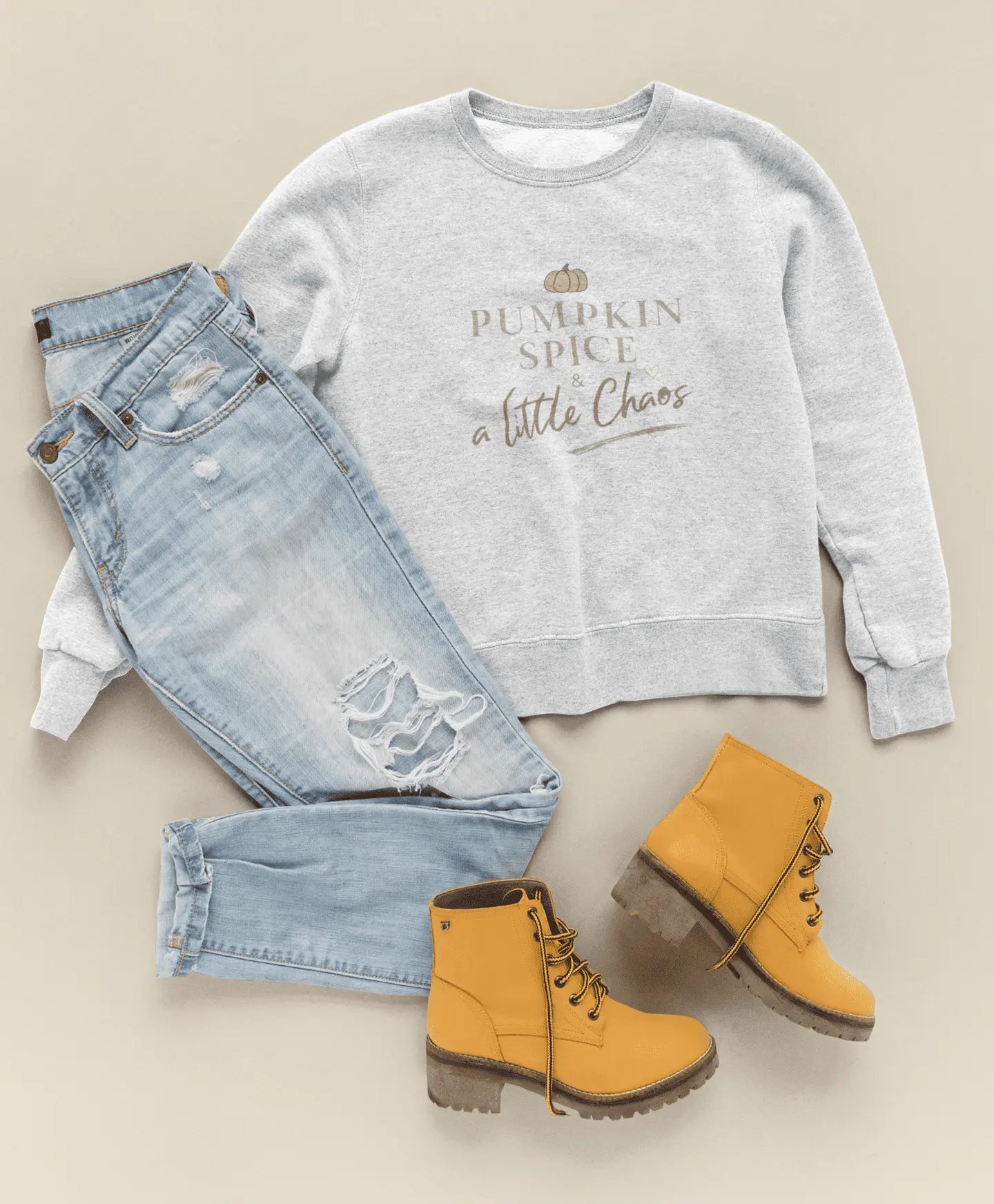 Gray sweatshirt with 'Pumpkin Spice and a Little Chaos' text, light blue jeans, and yellow boots on a beige background