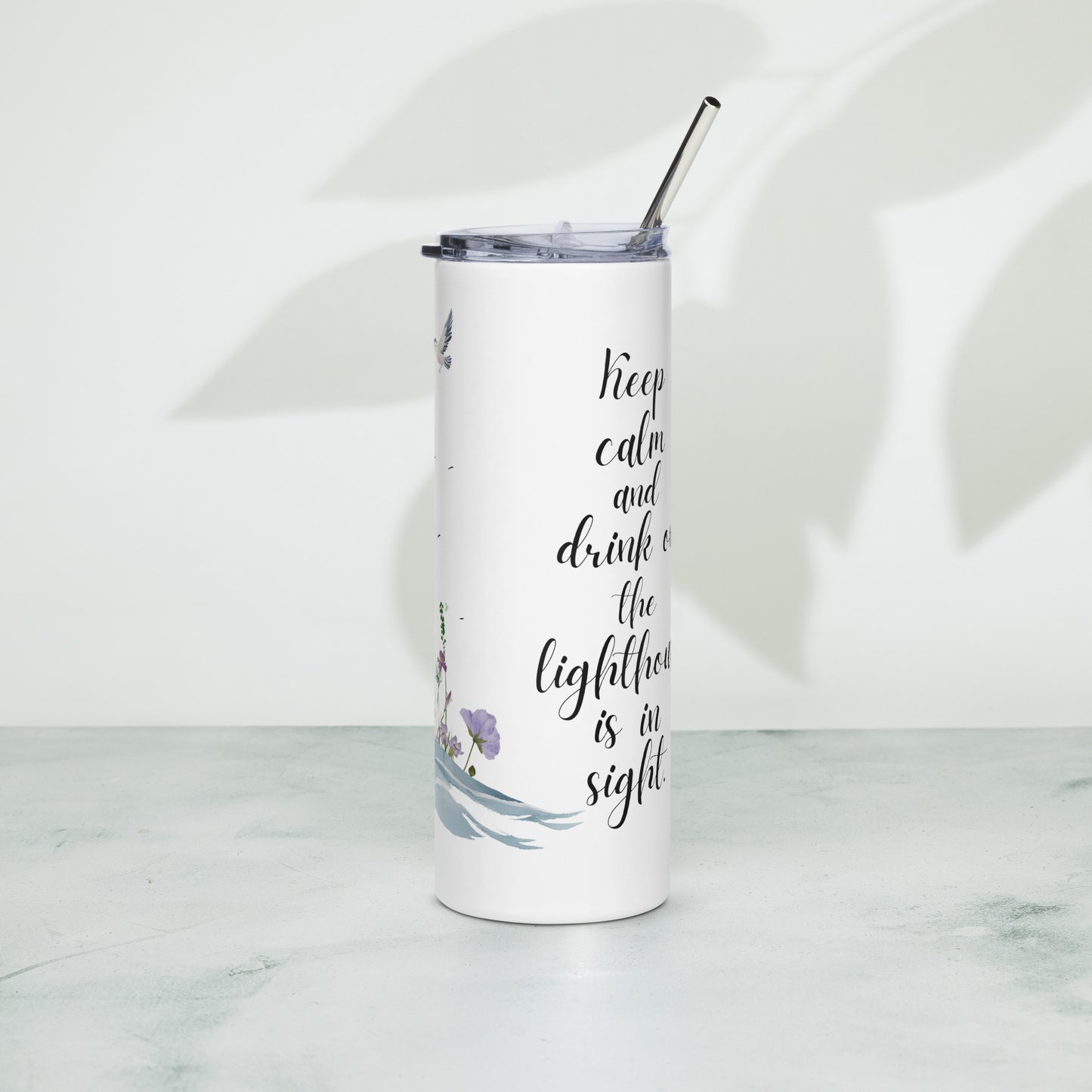 Stainless steel tumbler with a lighthouse-themed design and the phrase “Keep calm and drink on, the lighthouse is in sight,” standing on a textured surface with soft leaf shadows in the background.