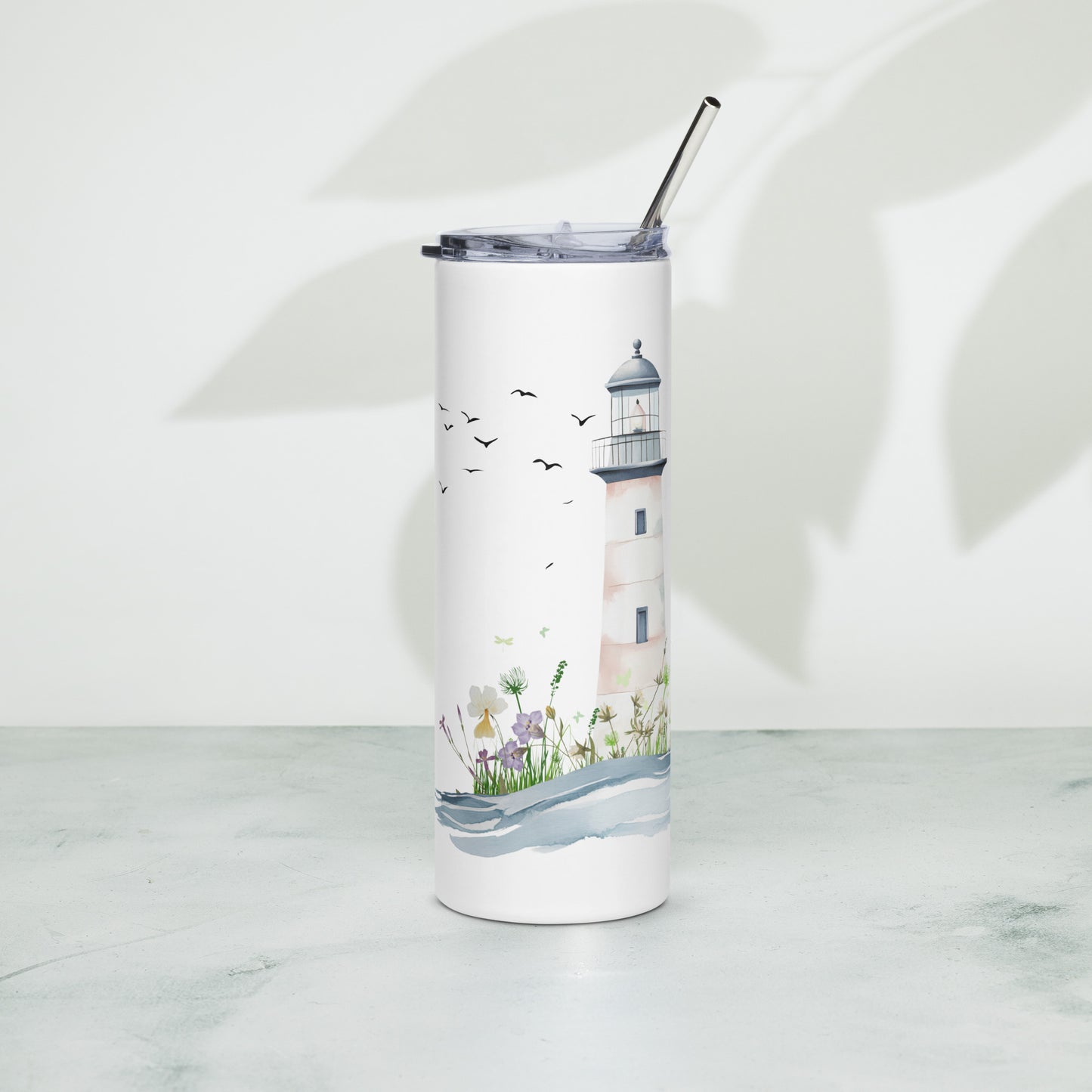White stainless steel tumbler with a pastel lighthouse illustration, soft waves, and wildflowers, placed on a light surface with gentle leaf shadows in the background.