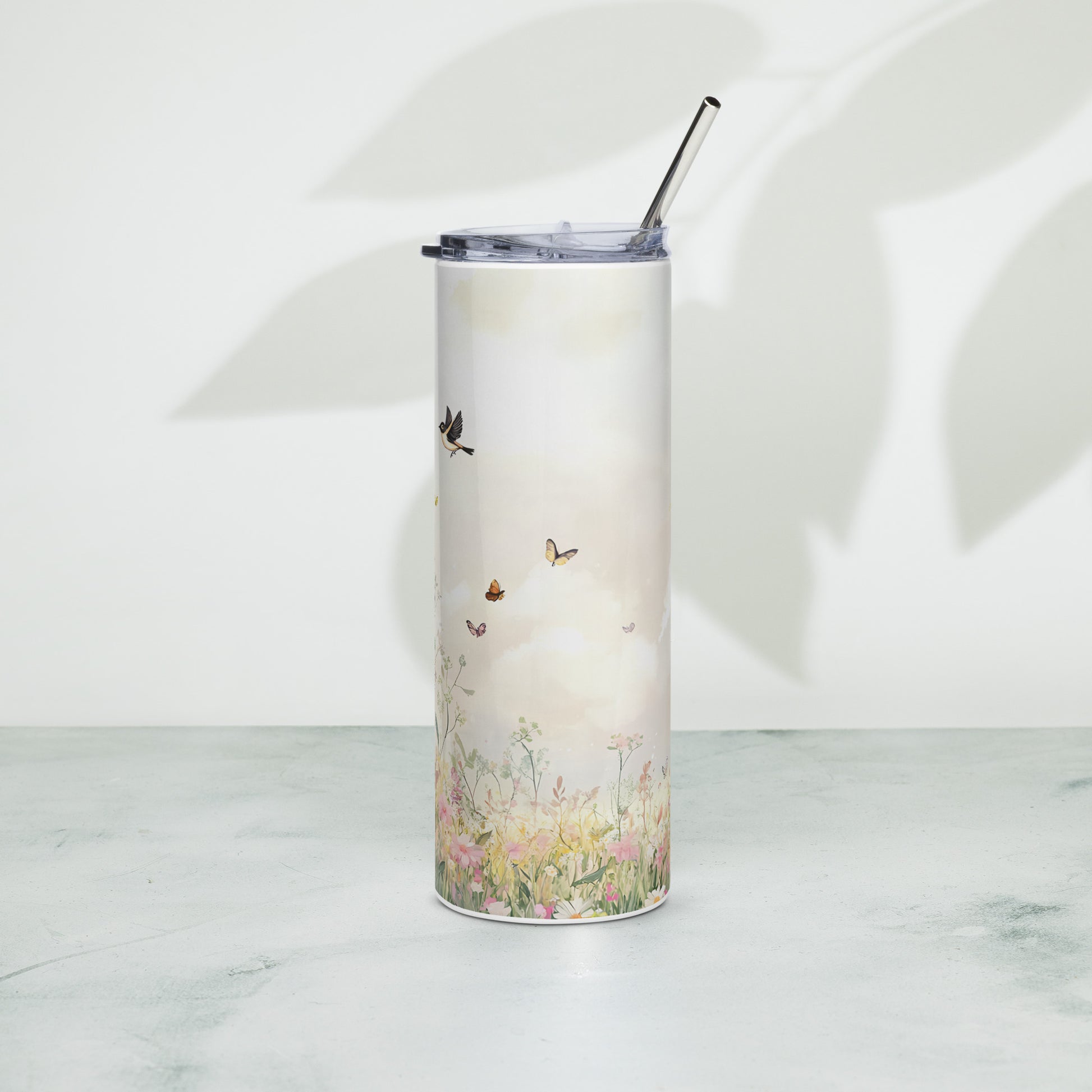 Tall pastel tumbler with floral meadow and butterflies, standing on a light surface with soft plant shadows in the background.