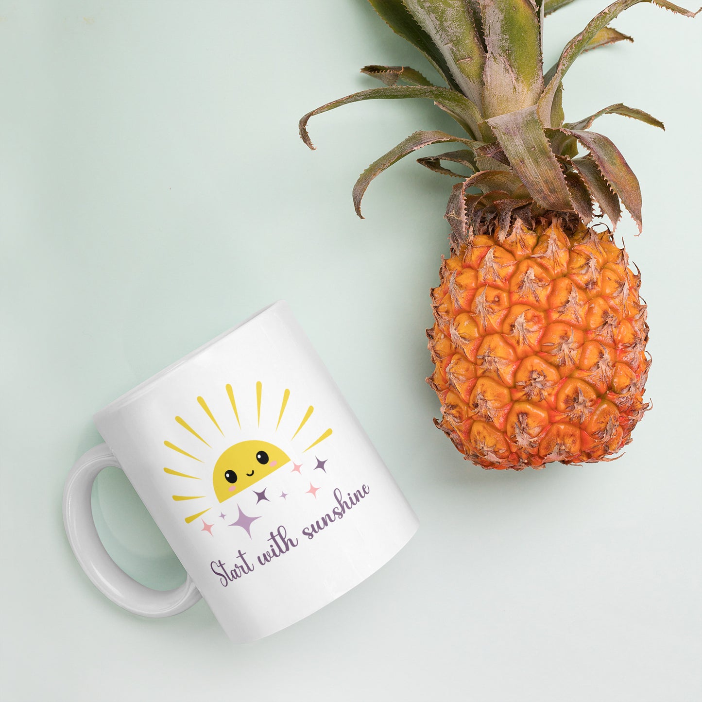 White coffee mug with smiling sun and sparkles, placed next to a fresh pineapple on pastel background — tropical summer flat lay with cozy morning vibes.