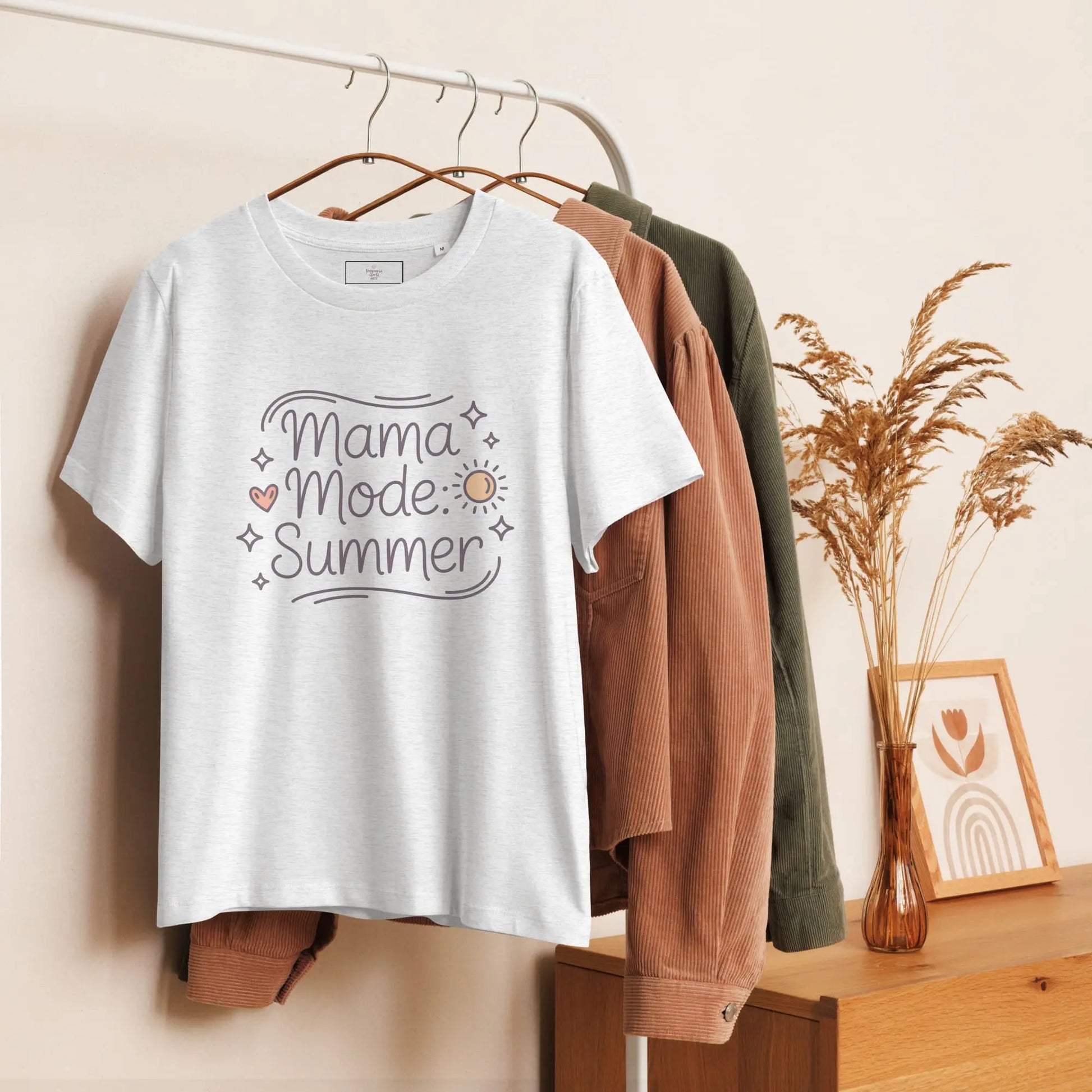 Hanging grey t-shirt with 'Mama Mode: Summer' design displayed on a wooden clothing rack with neutral decor.