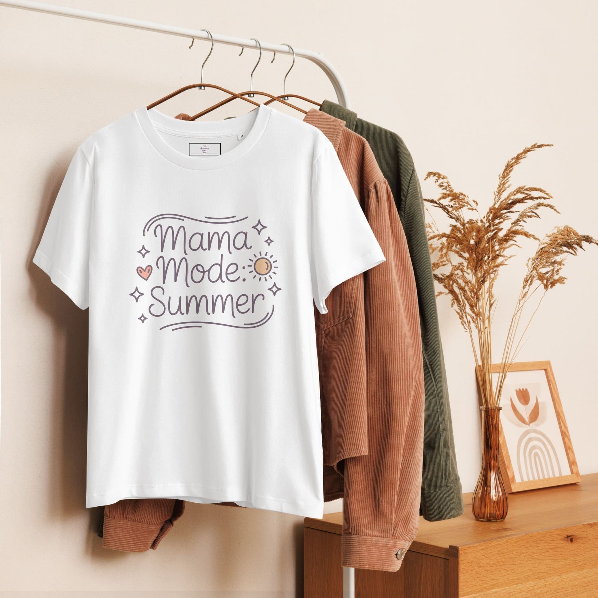 Hanging white t-shirt with 'Mama Mode: Summer' design displayed on a wooden clothing rack with neutral decor.