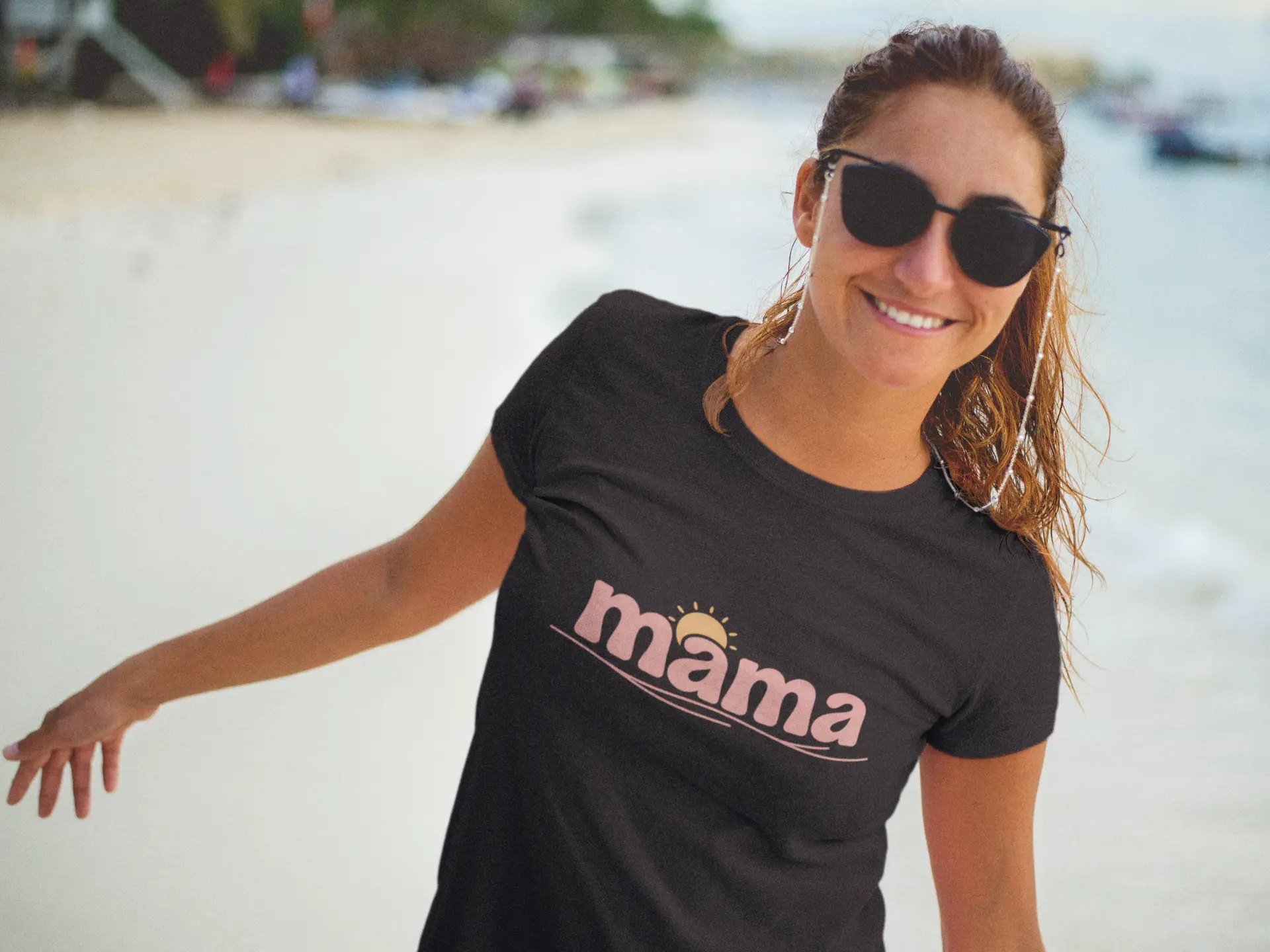Happy woman wearing black mama t-shirt with sunset design, styled for moms on summer beach day