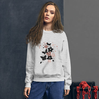 Woman wearing a light gray sweatshirt with a black and pink floral butterfly design on the chest, standing in front of a dark textured wall.