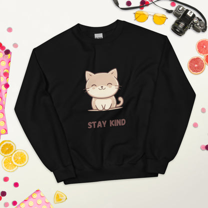 Black sweatshirt with a cute cat and the phrase “Stay Kind,” laid flat on a white surface, surrounded by colorful fruits, sunglasses, a camera, and playful decorative elements.
