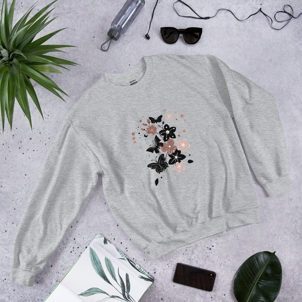 Flat lay of a sport gray sweatshirt with a black and pink floral butterfly design, styled with sunglasses, a water bottle, and leaves on a light stone background.