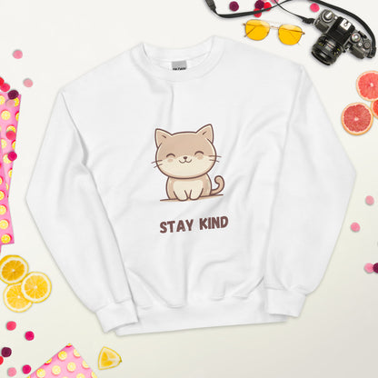 White sweatshirt with a cute cat and the phrase “Stay Kind,” laid flat on a white surface, surrounded by colorful fruits, sunglasses, a camera, and playful decorative elements.