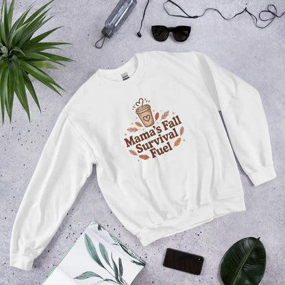 White sweatshirt with 'Mama's Fall Survival Fuel' text on a gray surface with accessories.