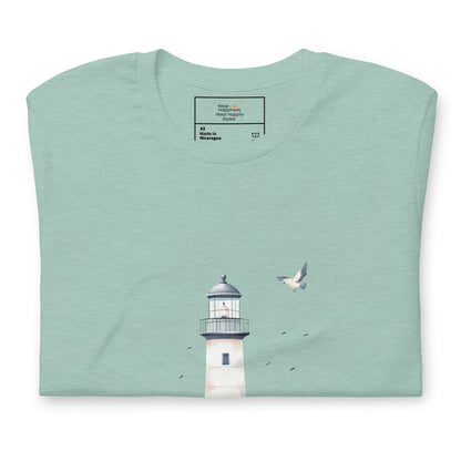 Flat-lay of a folded dusty blue-colored t-shirt featuring a minimal lighthouse and seagull design, styled for a calming, nature-inspired mom aesthetic.